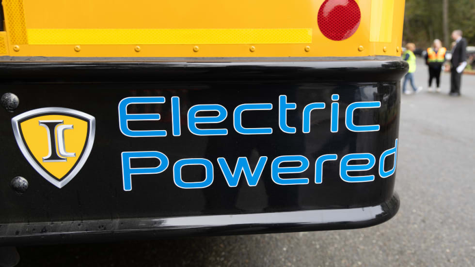 The back right corner of a school bus with blue text on the bumper reading "Electric Powered". 