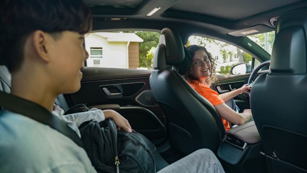 Female HopSkipDrive CareDriver in an orange shirt driving a student to school in a car.