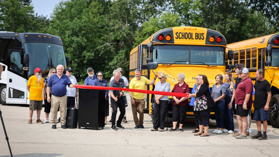 A crowd stands behind a red ribbon being cut.