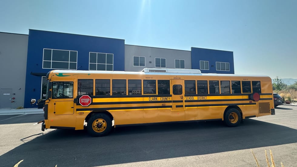 A yellow Blue Bird electric school bus sits in front of a school building.