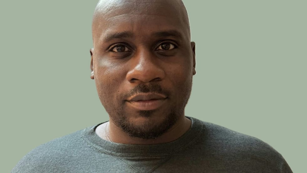 Bald man in gray sweater against sage green background