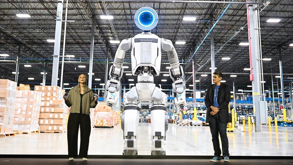 Boston Dynamics executives in front of image of Atlas humanoid robot in a warehouse setting