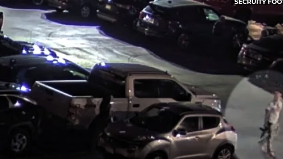 Night security footage of parking lot with multiple vehicles and blue emergency lights