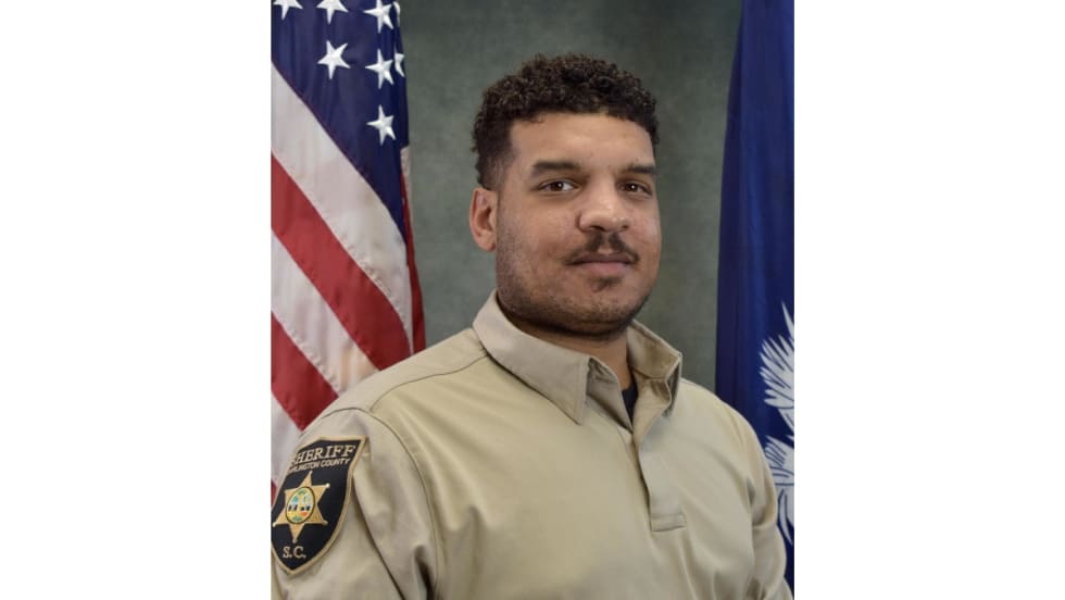 Sheriff's deputy in tan uniform posing with American and state flags