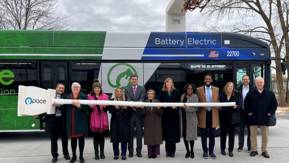 A group of people pose in front of a battery electric transit bus.