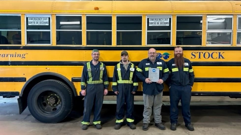 four men stand in front of a school bus