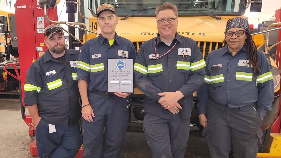 Durham School Services Ann Arbor team with ASE Blue Seal of Excellence plaque in front of a school bus