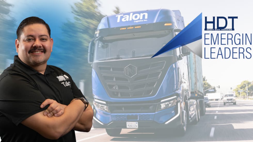 Hispanic man stands with arms crossed with electric Nikola truck in the background