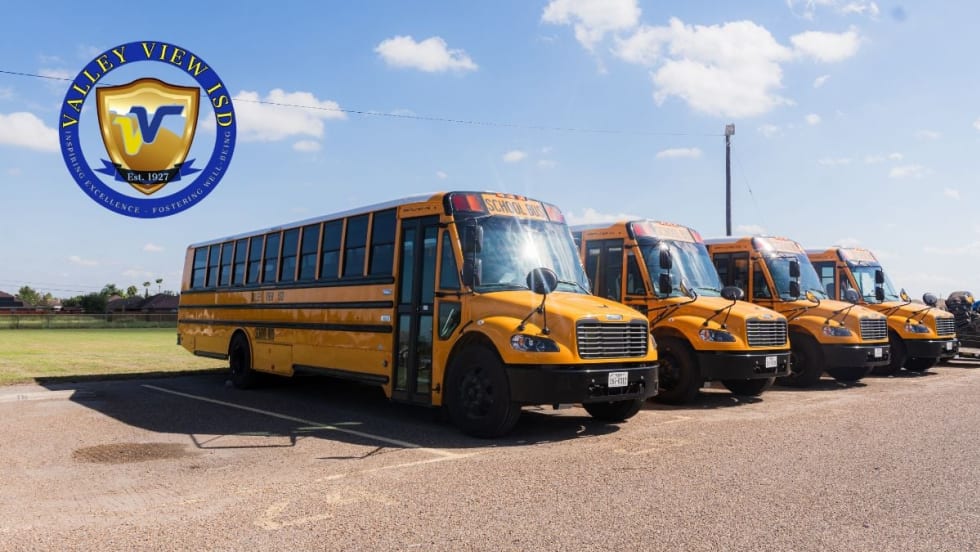 A row of yellow Valley View ISD electric school buses parked outdoors with the district logo in the corner of the image.