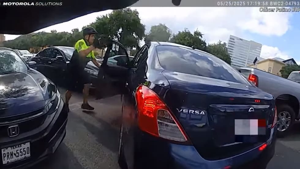 Dashcam view of traffic stop with police officer near dark blue Nissan Versa