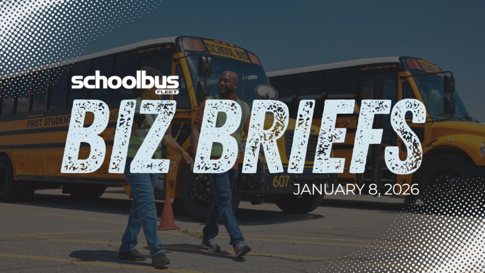 Image of two people in high visibility vest walking in front of parked school buses with text reading "Biz Briefs."