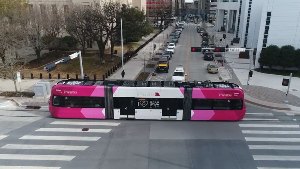 An pink and white OKC streetcar moves down a street.