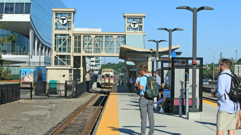 Commuter rail riders wait on a station platform.