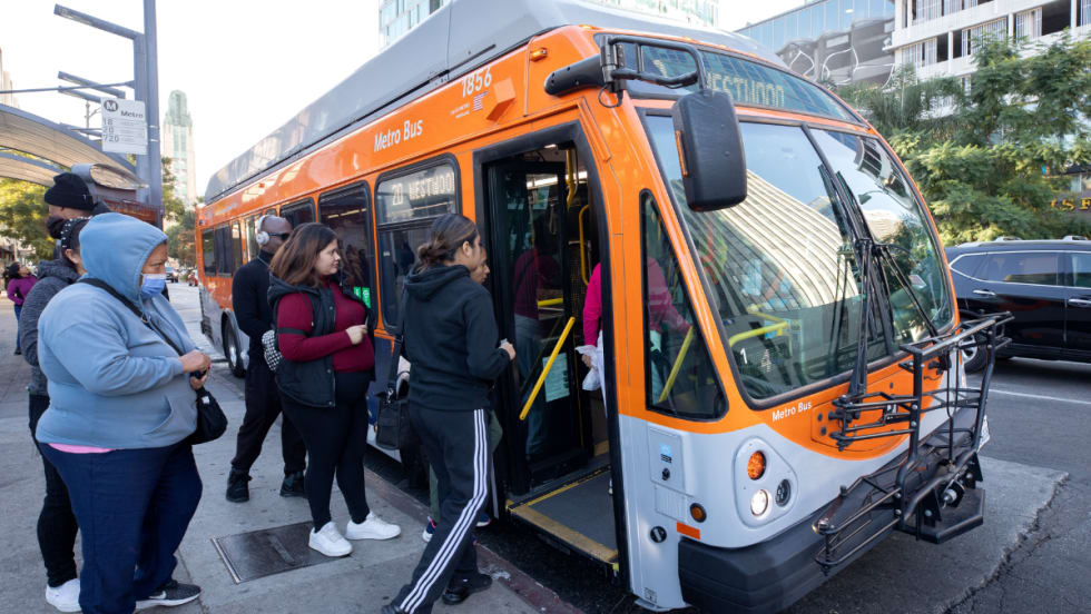 Riders board an orange and gray LA Metro bus.