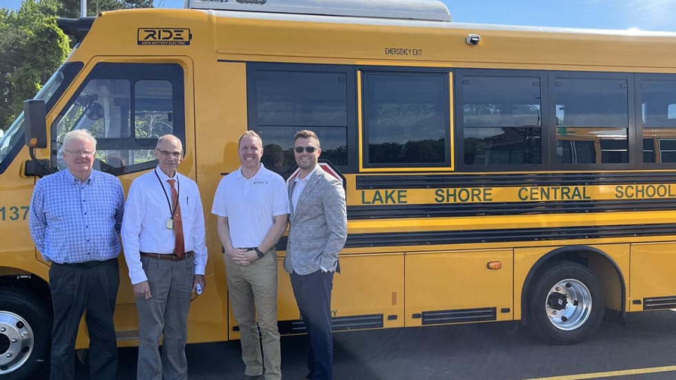 District official posing with a RIDE electric school bus. 