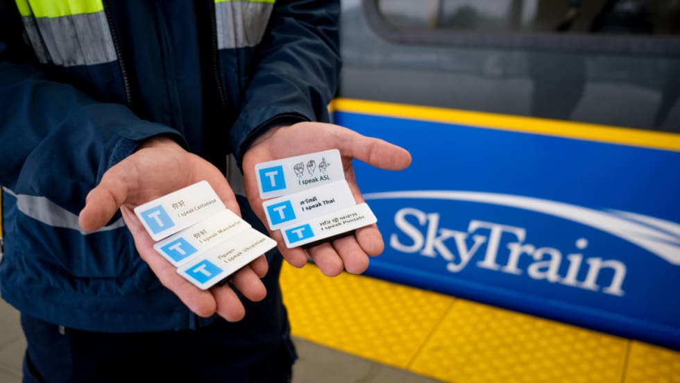 A TransLink SkyTrain worker holds up 6 language pins.