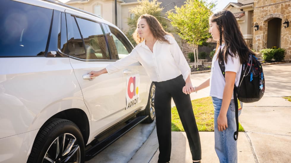 An Adroit driver opening a car door for a student.