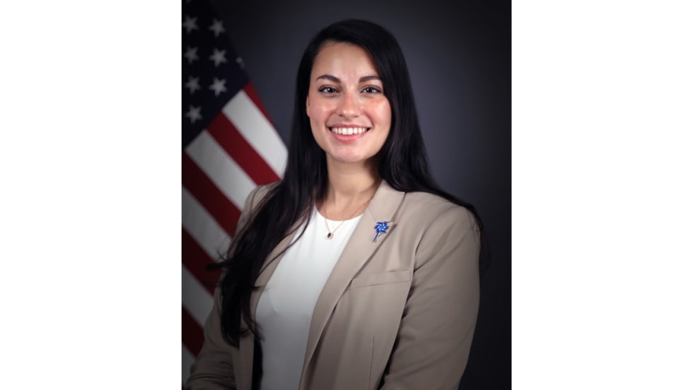 Smiling professional woman in beige blazer standing in front of American flag