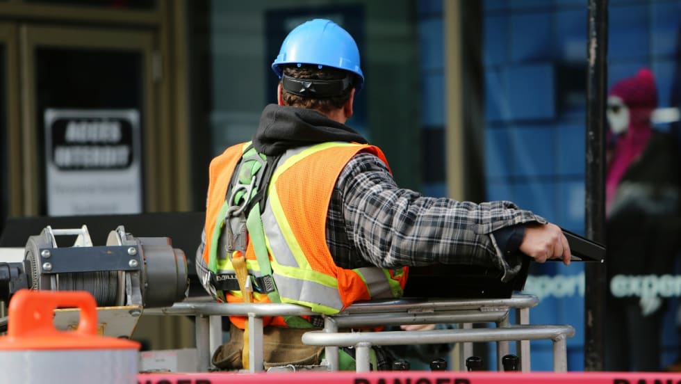 The back of a construction worker wearing a blue hard hat and an orange visibility vest.