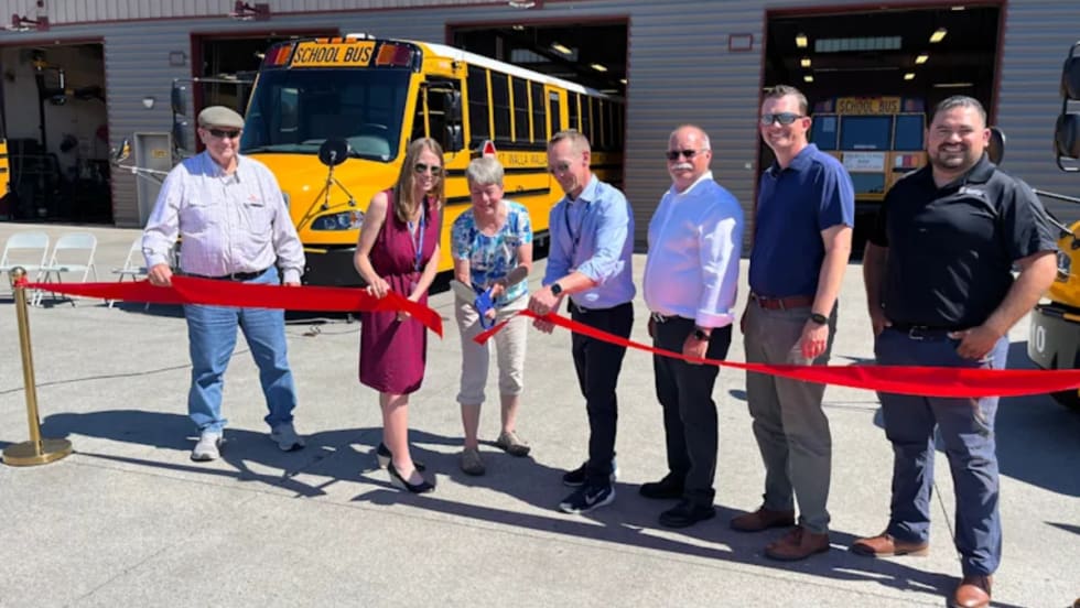 School officials cutting a red ribbon in front of electric school buses.