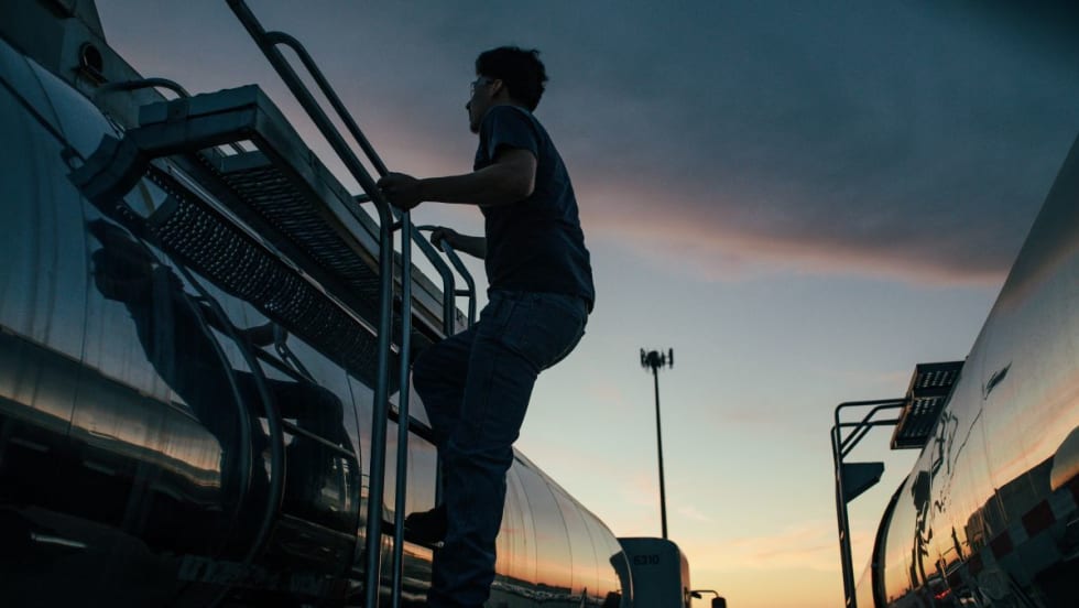 Truck driver climbs side of tanker trailer at sunset or sunrise