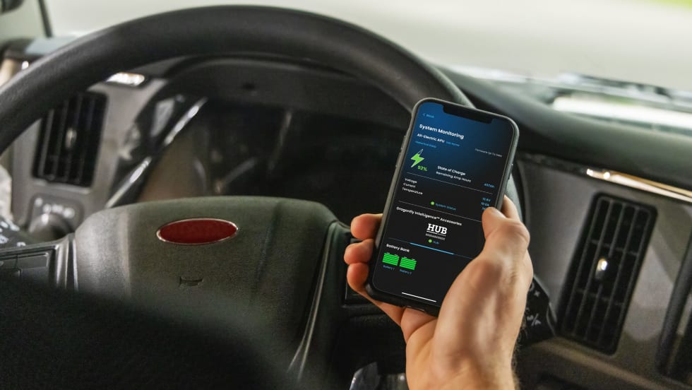 Truck driver holding phone in hand with Battle Born app monitoring lithium batteries.