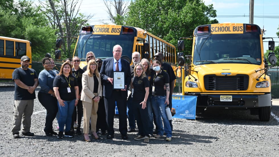 A group poses with two Thomas Built Buses Safe-T-Liner C2 Jouley electric school buses parked outside.