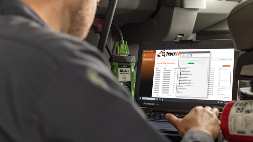 Technician using Truck Check-Up diagnostic software on a Panasonic Toughbook laptop inside a truck cab