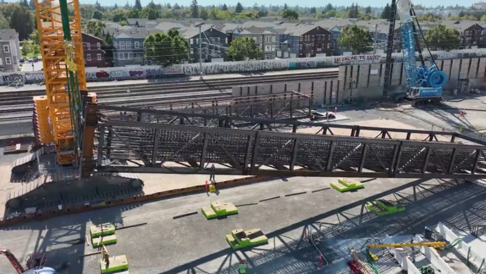 A large yellow crane lifts a steel rebar cage on one side.