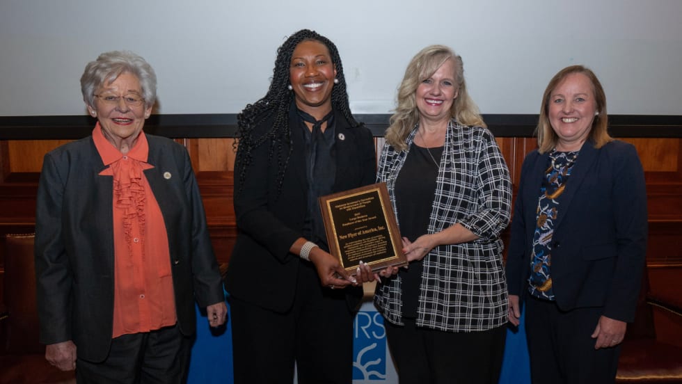 Four women pose for a group photos with the New Flyer award plaque.