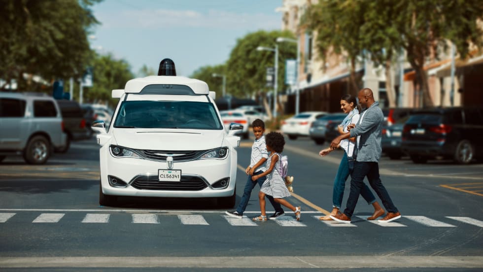 A white Waymo vehicle waits at a crosswalk as a family crosses.