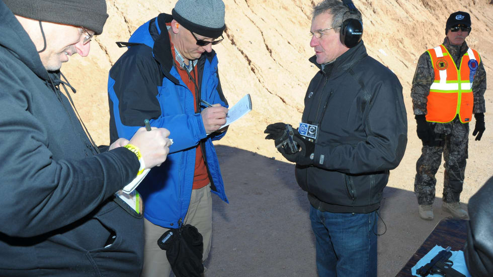 Group of professionals in winter gear examining documents near rocky terrain