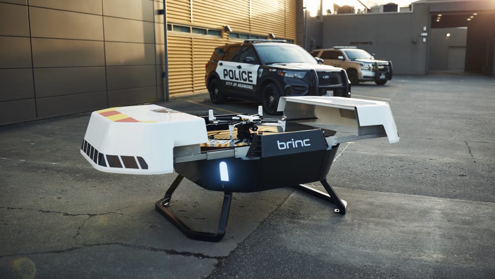 A Responder drone sits atop a Responder Station charging nest with two law enforcement vehicles in the background.