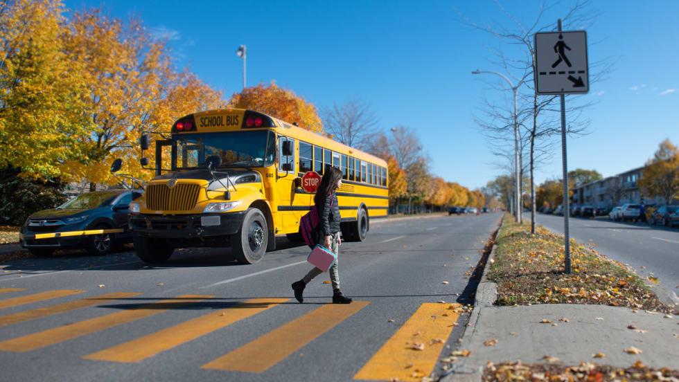 A student crosses the street in front of a school bus.