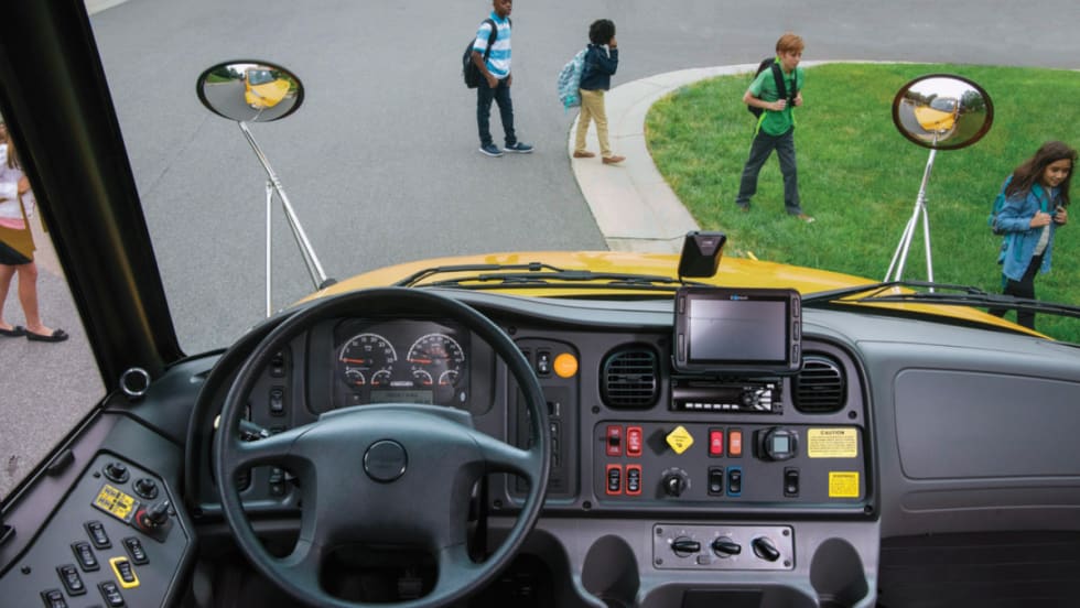 Inside view of a bus driver seat with students walking across the road.