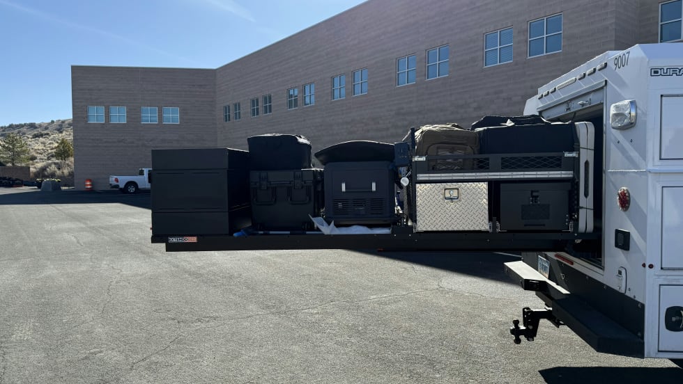 White emergency response vehicles parked beside gray building on asphalt lot
