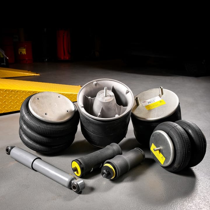 A collection of vehicle suspension components including air springs, bellows, and a shock absorber, arranged on a workshop floor.