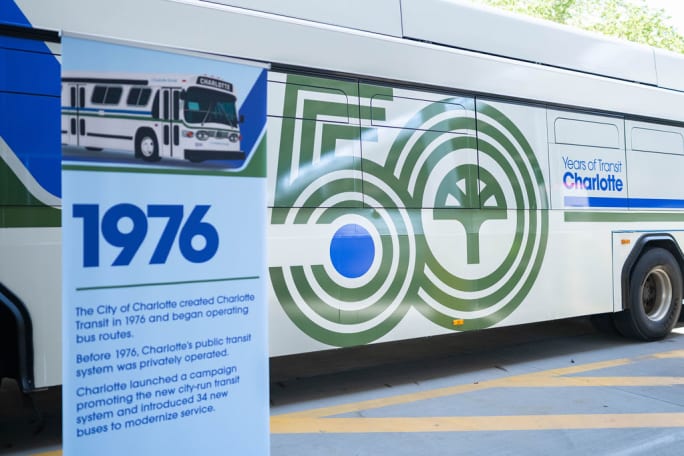 A sign detailing CATS history from 1976 with a newly wrapped transit bus in the background celebrating 50 years.