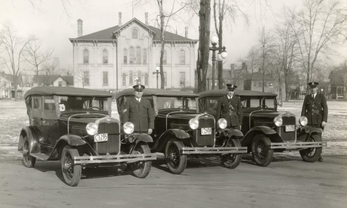 1930s police vehicles with officers standing beside vintage automobiles in urban setting