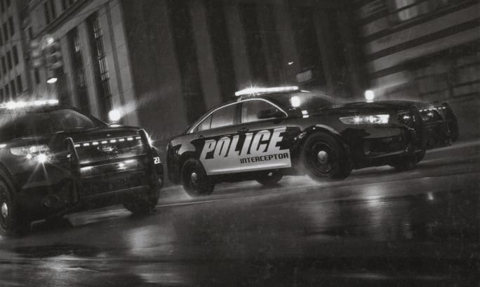 Black and white police interceptor vehicles in urban nighttime street scene
