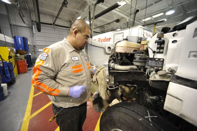 A technician looking at a laptop in front of a heavy-duty truck.