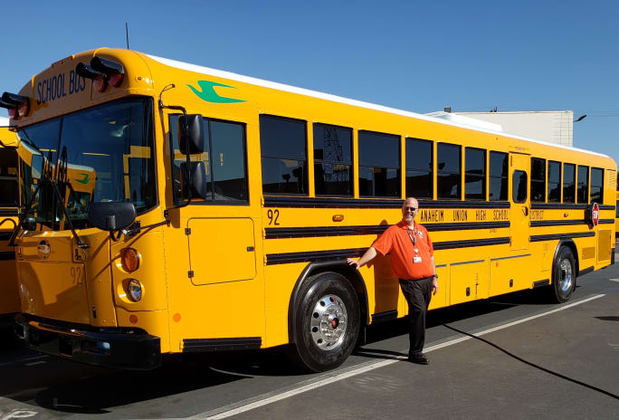 A Type D Blue Bird bus with a man posing in front of it.