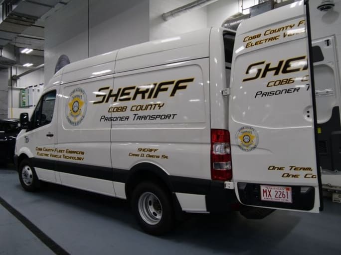 A white electric cargo van is shown with the Cobb County Sheriff's Office logo and badge on the sides.