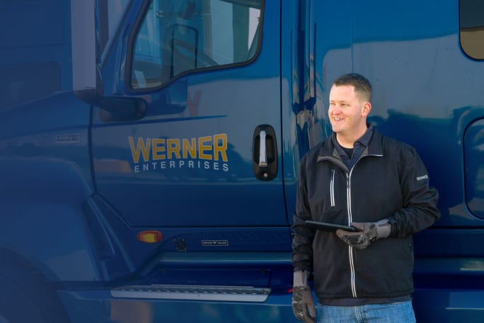 Truck driver holding tablet standing next to blue Werner Enterprises truck