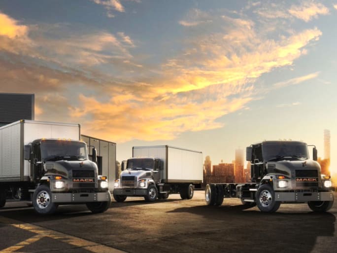 Three medium-duty trucks with black cabs are parked in front of the sky at sunset. Two are box trucks and one is a chassis cab.