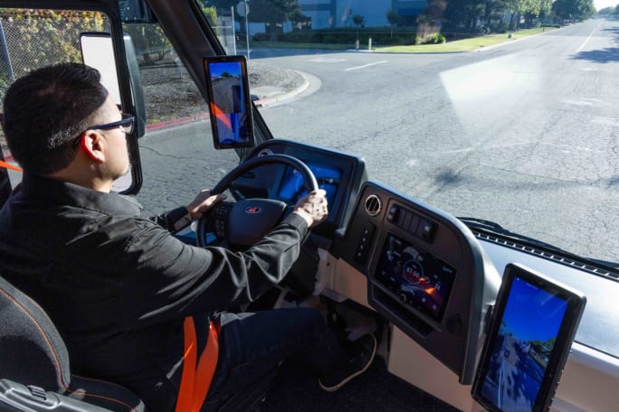 View over the shoulder of a driver driving a futuristic-looking electric truck.