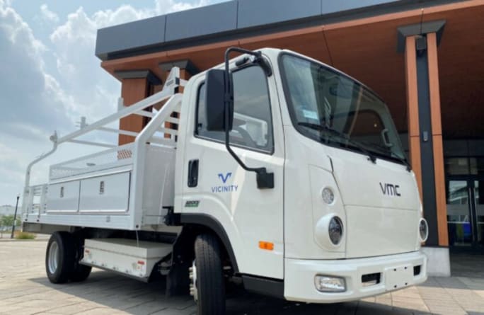Ana electric truck with a white cab and white service body parked in front of a building.