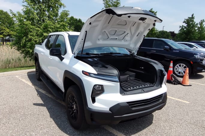 The front of a white EV work truck is opened to reveal storage under the hood.