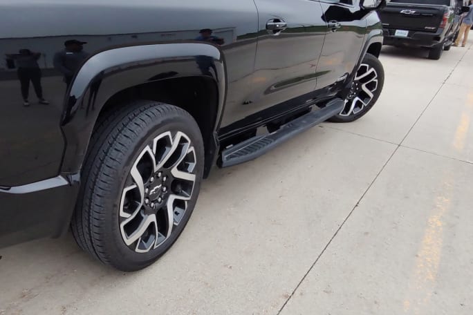 view of the lower half of a black pickup truck, side view, with front tires turned to the right and rear tires turned slightly