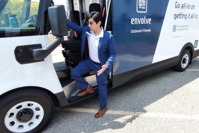 Man in blue suit climbs into the driver-side entry of a white and blue cargo van.